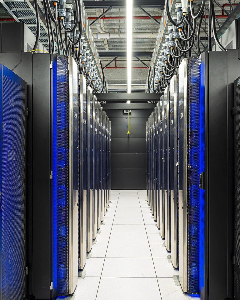 A technician walking between racks of supercomputer hardware